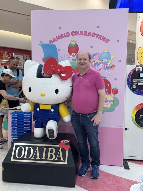 Moi, portant une chemise violette et des jeans Le Temps des Cerises, à côté d'une statue de Hello Kitty