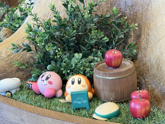 Kirby et Waddle Dee assis avec des toques à leurs côtés, ainsi qu'un fǔt avec une pomme en haut.