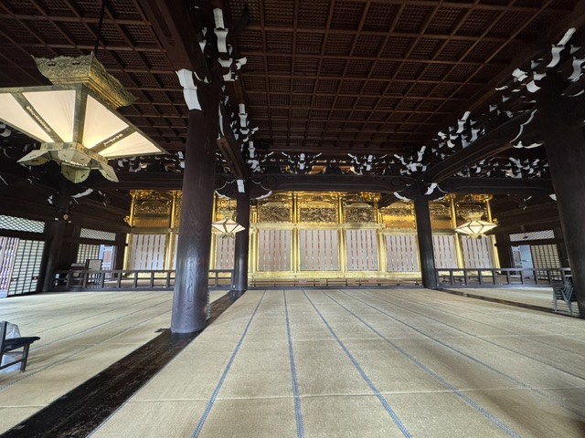 Intérieur de la salle -- plafond en bois noir, des tapis de prière partout, et des lanternes suspendues du plafond
