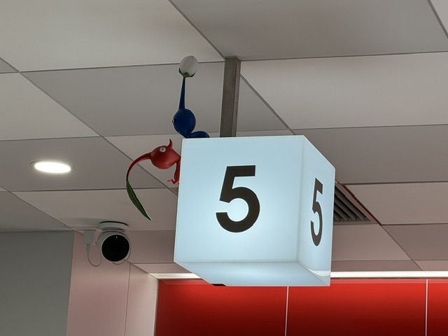 Une cuve blanche avec le numéro 5 en noir -- des Pikmin rouge et bleu marchent au-dessus