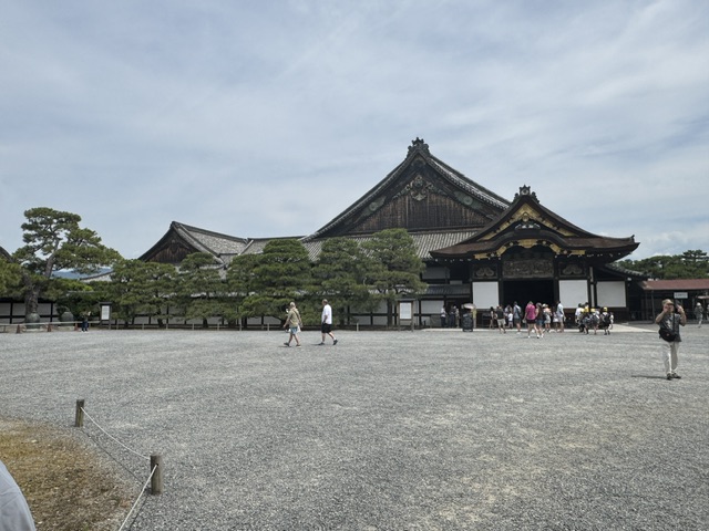 Grande cour recouverte de cailloux gris. En arrière-plan, il y a un grand bâtiment avec des toits courbés, du style japonais traditionnel