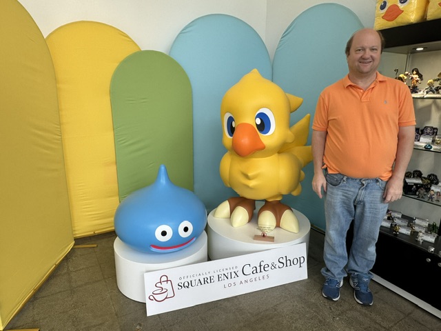 Moi, portant un polo orange et un jean, à côté d'une statue de Chocobo et Slime