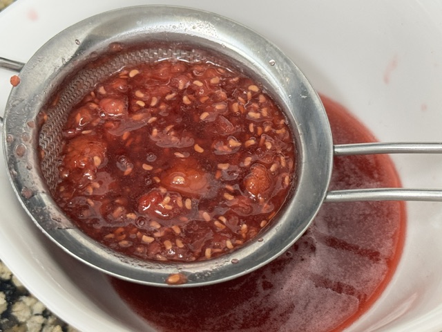 Tamis plein de graines de framboise -- le sirop est visible dans le bol