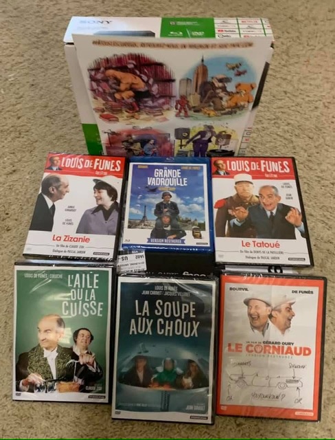C'est six DVDs, de gauche à droite et de haut en bas : La Zizanie, La Grande Vadrouille, Le Tatoué, L'Aile ou la cuisse, La Soupe Aux Choux, Le Corniaud. Derrière le disques, il y a un lecteur universel (acheté aux É-U) et une affiche de la FNAC, gratuite dans le colis