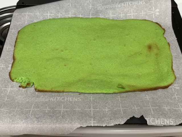 Couche de gâteau vert posée sur la plaque de cuisson avec du papier au-dessous