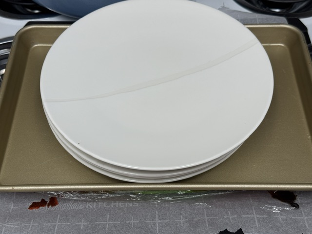 Plaque de cuisson posée en haut du gâteau emballé. Il y a 5 assiettes posées en un tas au-dessus de la plaque.