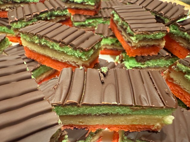 Gros plan d'une assiette pleine de cookies arc-en-ciel. Ils sont rouge au fond, nature au centre, vert vers le haut, et couvert avec du chocolat.