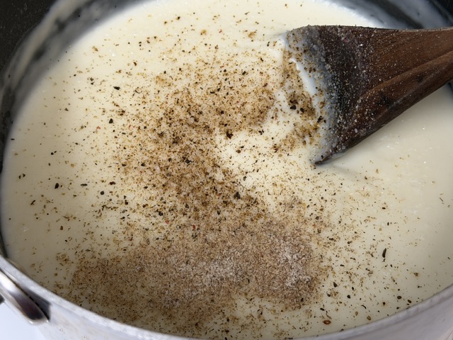 Sauce béchamel dans une casserole, avec de sacrées quantités de muscade râpée et de poivre moulu sur la surface