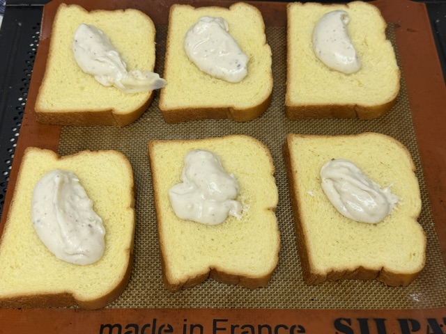 6 tranches de pain sur une plaque de cuisson, avec des tas de béchamel sur chacune
