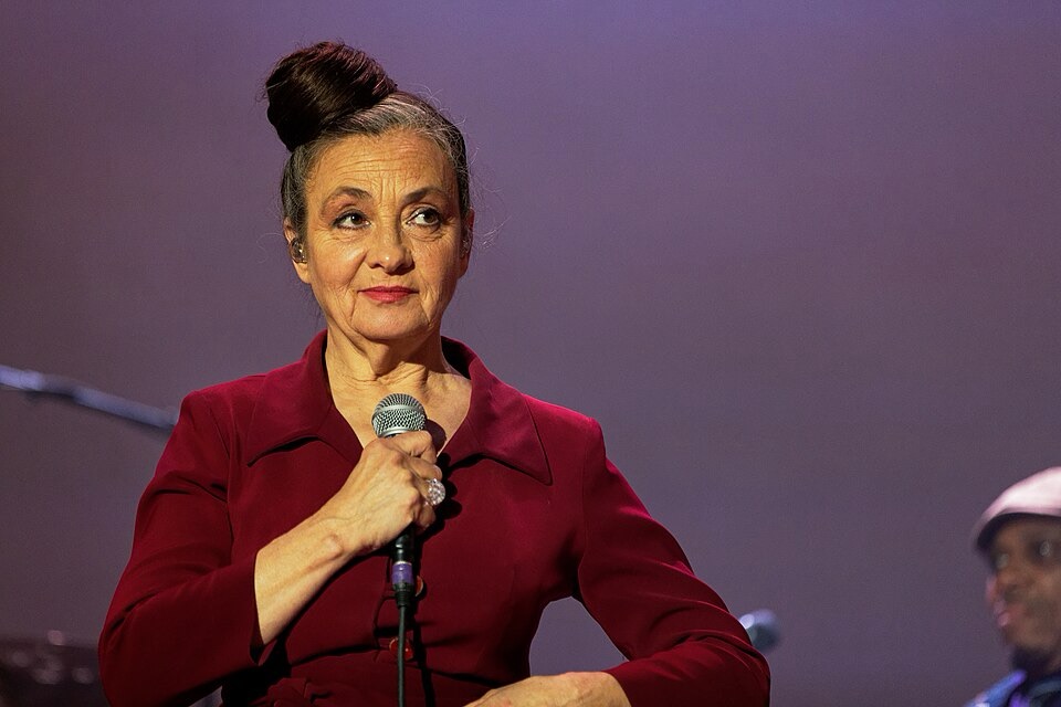 C'est Catherine Ringer dans une robe rouge, les cheveux en chignon. Elle tient un micro dans la main droite sous sa tête.