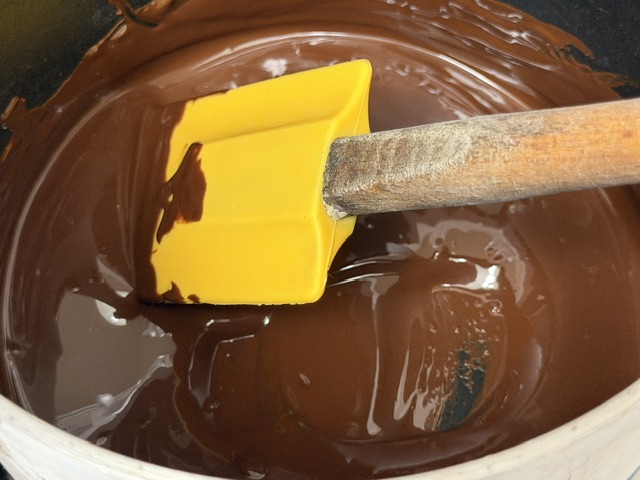Chocolat fondu dans la casserole. Une maryse avec une tête jaune est posée au centre