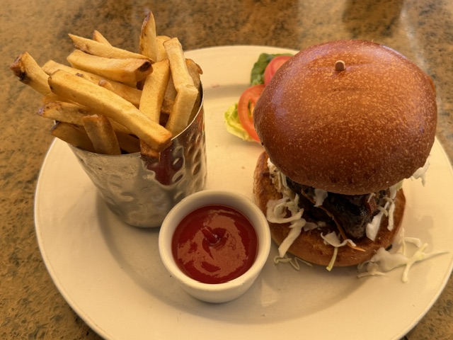 Vue de l'ensemble, un pain brioché avec une belle quantité de plat de côte, une tasse de frites, et du ketchup dans un petit ramequin.