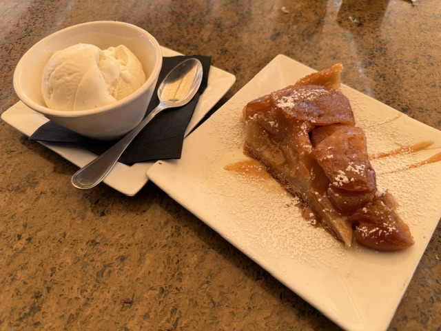 À gauche, une coupe de glace à la vanille. À droite, une tranche de tarte Tatin, avec du caramel versé sur l'assiette, légèrement saupoudrée de sucre glace.