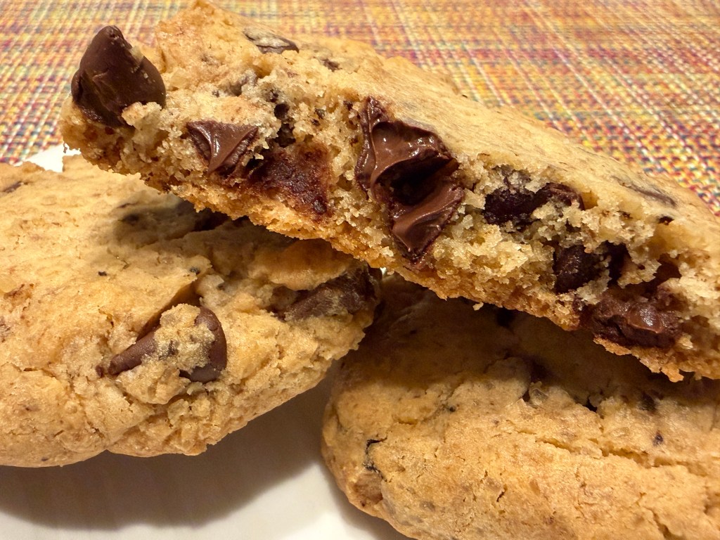 Gros-plan de la moitié d'un cookie pour voir l'intérieur, posé au-dessus de dux cookies entiers sur une petite assiette blanche.